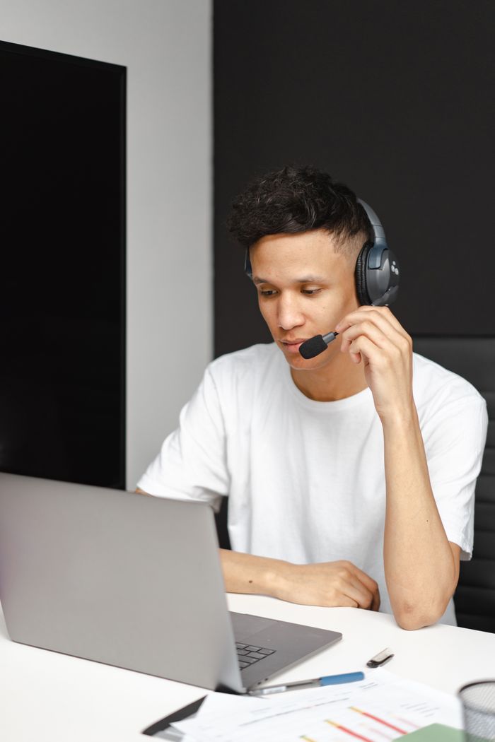 Support agent wearing headset working on a laptop in modern office setting.