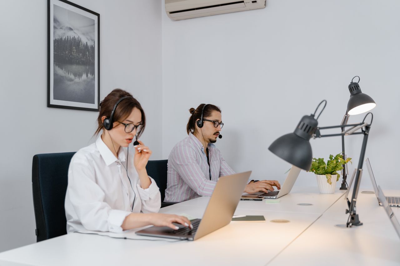 Two call center agents using laptops and headsets in a modern office setting.