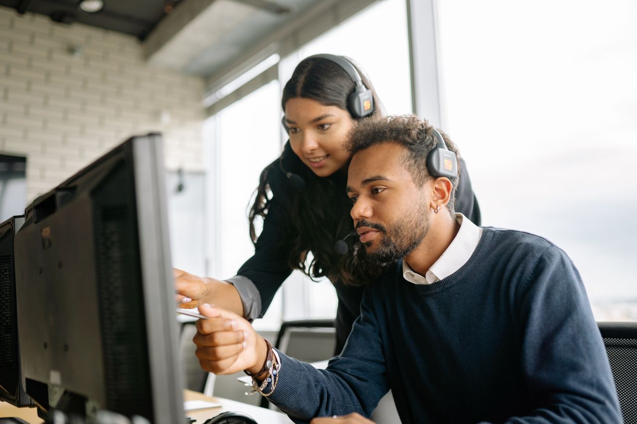 Two call center employees working together with headsets in a modern office setting.